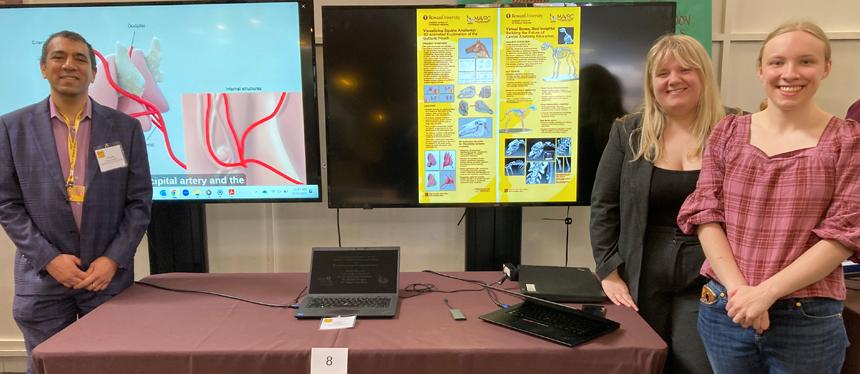 Faculty and Students stand in front of virtual reality poster and television display at research competition